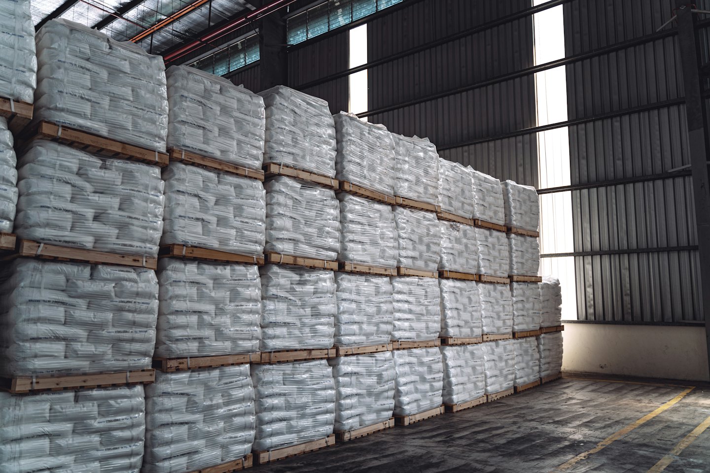 White bags stacked on pallets in a large warehouse.
